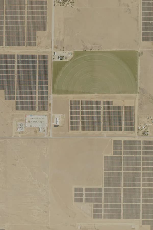 Aerial view of a solar park, with rows of panels beside an irrigated field and a substation